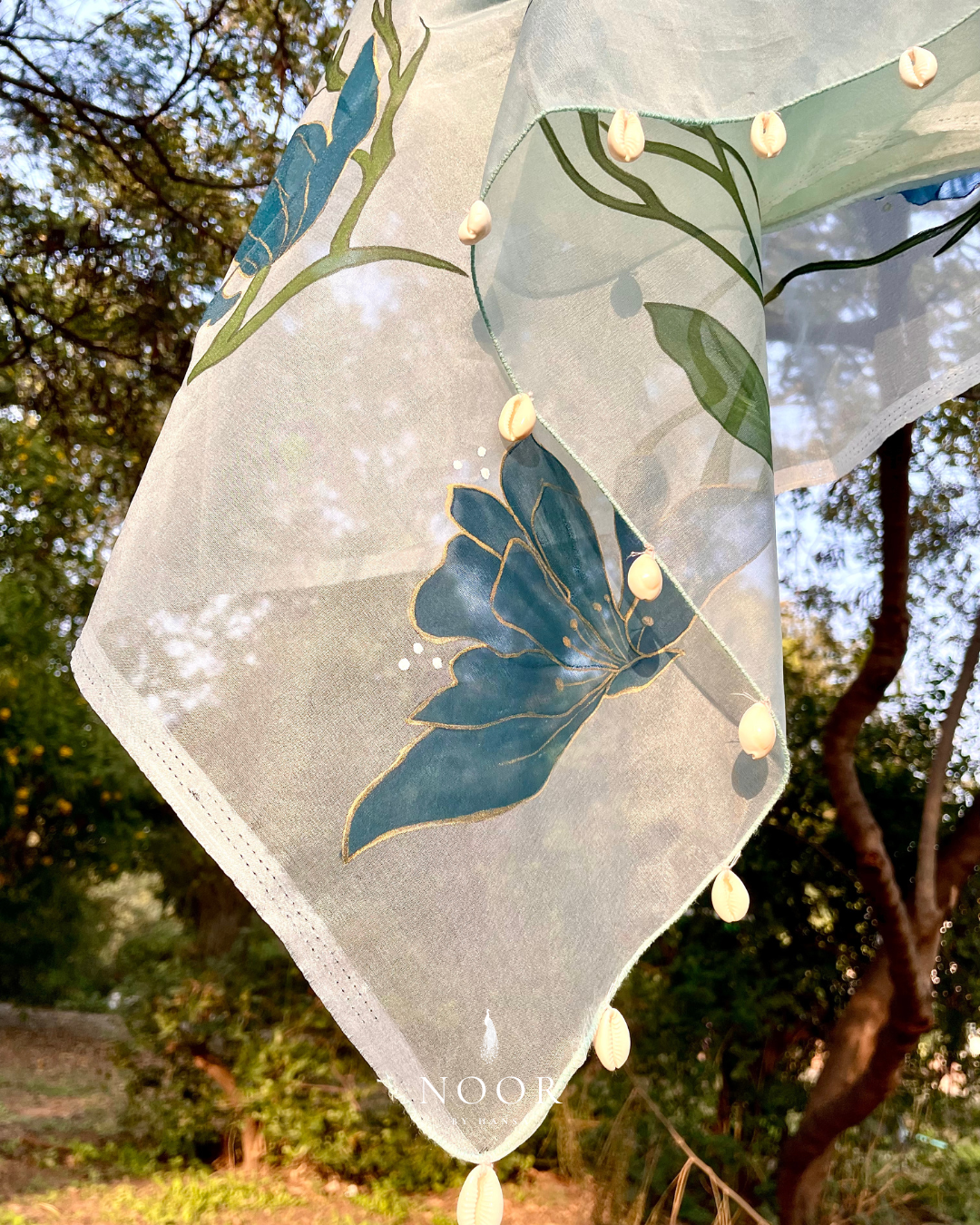 hand painted saree in pure organza silk by noor by hansa in teal colour paired with a pure cotton blouse piece, shells on the pallu