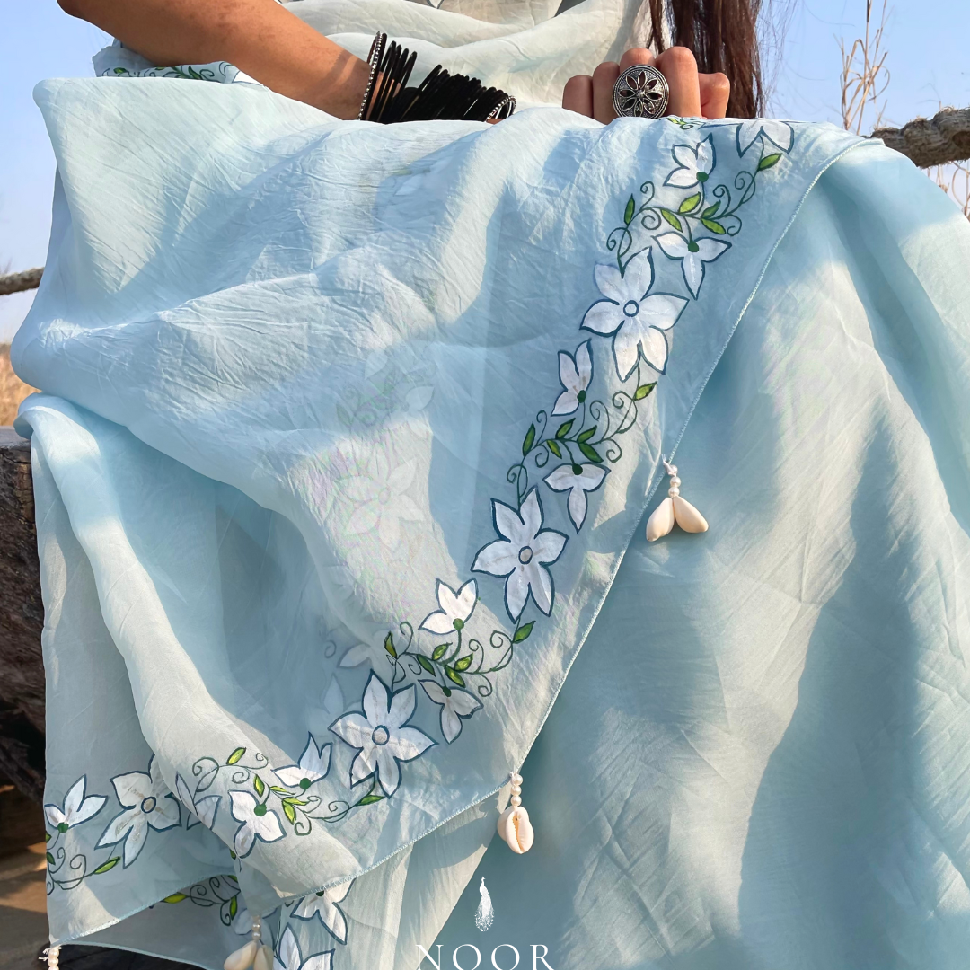 hand painted saree in pure organza silk by noor by hansa in blue colour paired with a pure cotton blouse piece, shells on the pallu