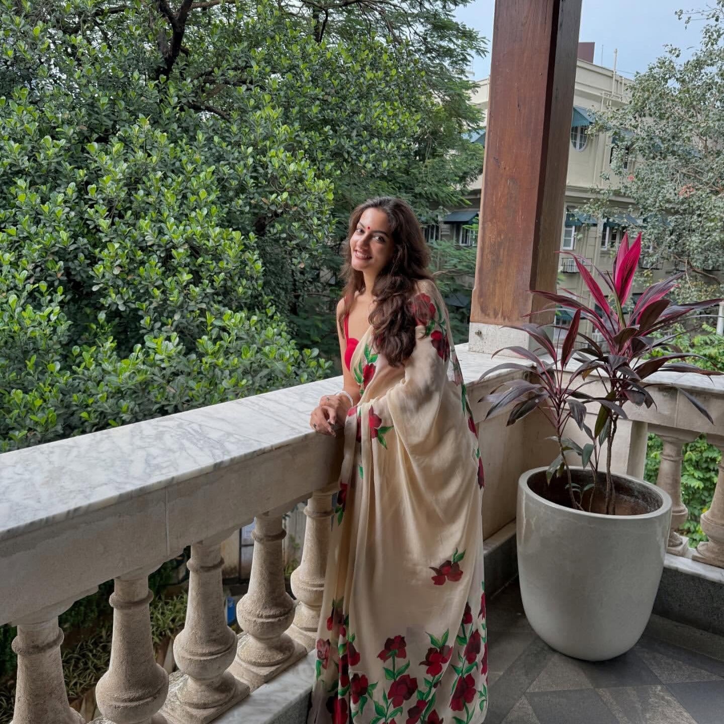 Woman in a floral saree standing on a balcony with greenery in the background