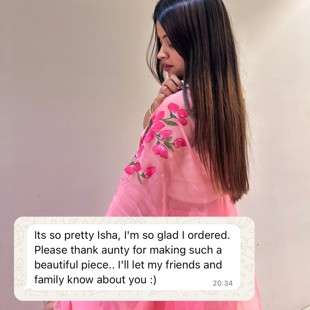 Woman wearing a pink saree with floral patterns, standing against a plain background.