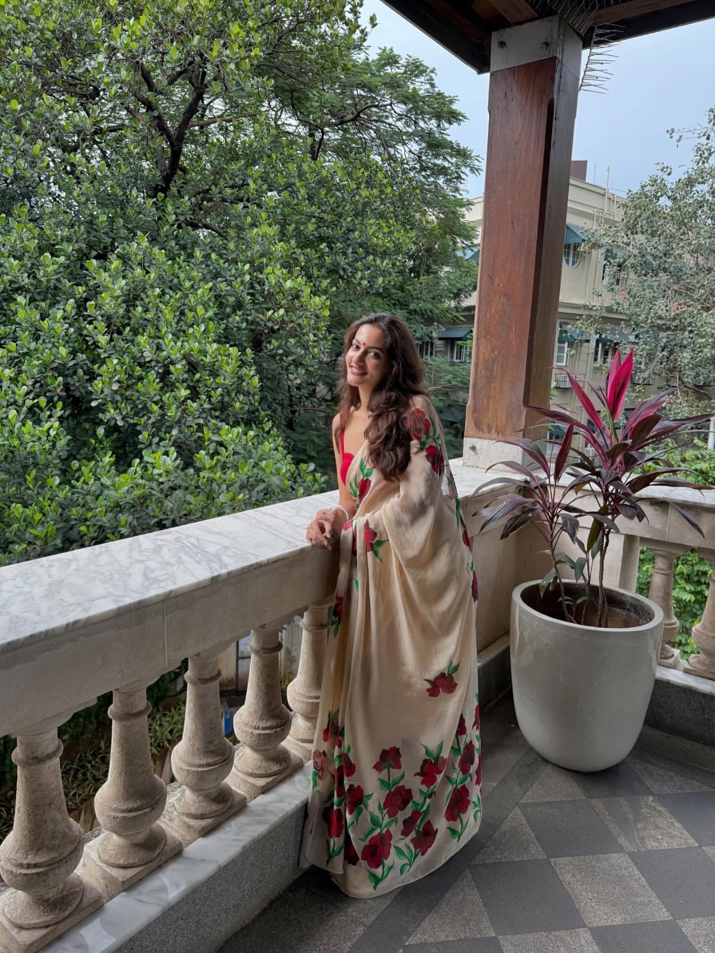 Woman in a floral saree standing on a balcony with greenery in the background